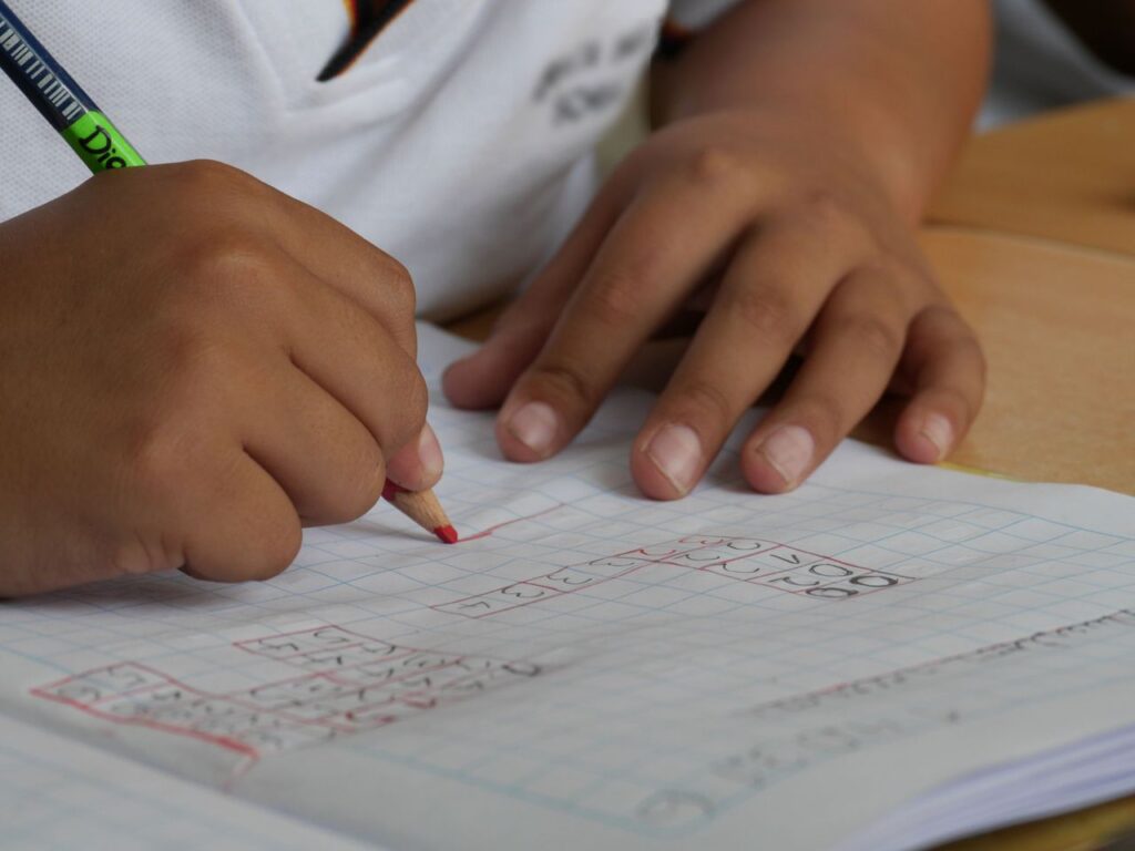 Close-up of a student writing math equations in a notebook with a pencil indoors.